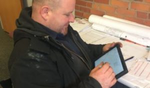 Technician wearing black jacket, filling out form on an iPad.