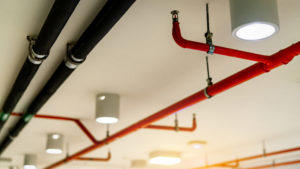 Automatic fire sprinkler safety system and black water cooling supply pipe. Fire Suppression. Fire protection and detector. Fire sprinkler system with red pipes hanging from ceiling inside building.